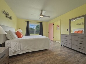 A bedroom with a bed, a dresser, a ceiling fan, and a door leading to another room. - Pastel Place | Colorful 3BR Tulsa Duplex (Tulsa)
