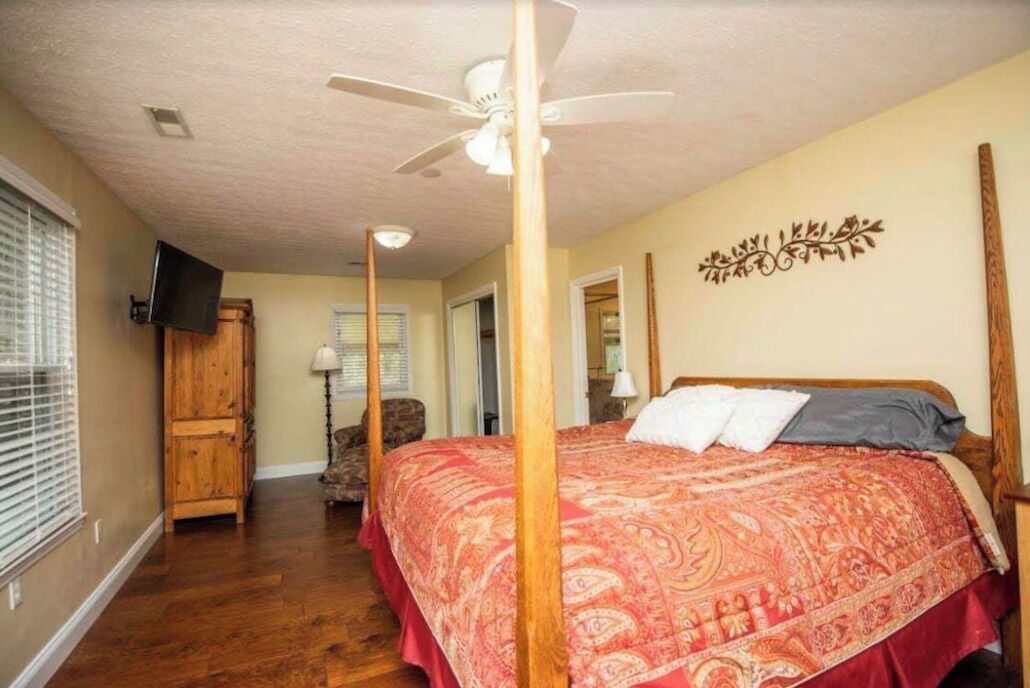 Une chambre à coucher avec un lit à baldaquin, un ventilateur de plafond, un téléviseur fixé au mur et une armoire en bois.