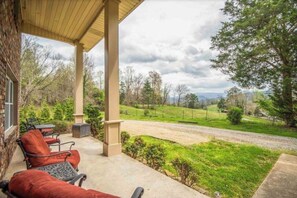 A covered patio with outdoor furniture, a view of a grassy area, and a road in the background. - Entire Home in Townsend w/HOT TUB and Stunning Mtn Views (Townsend)