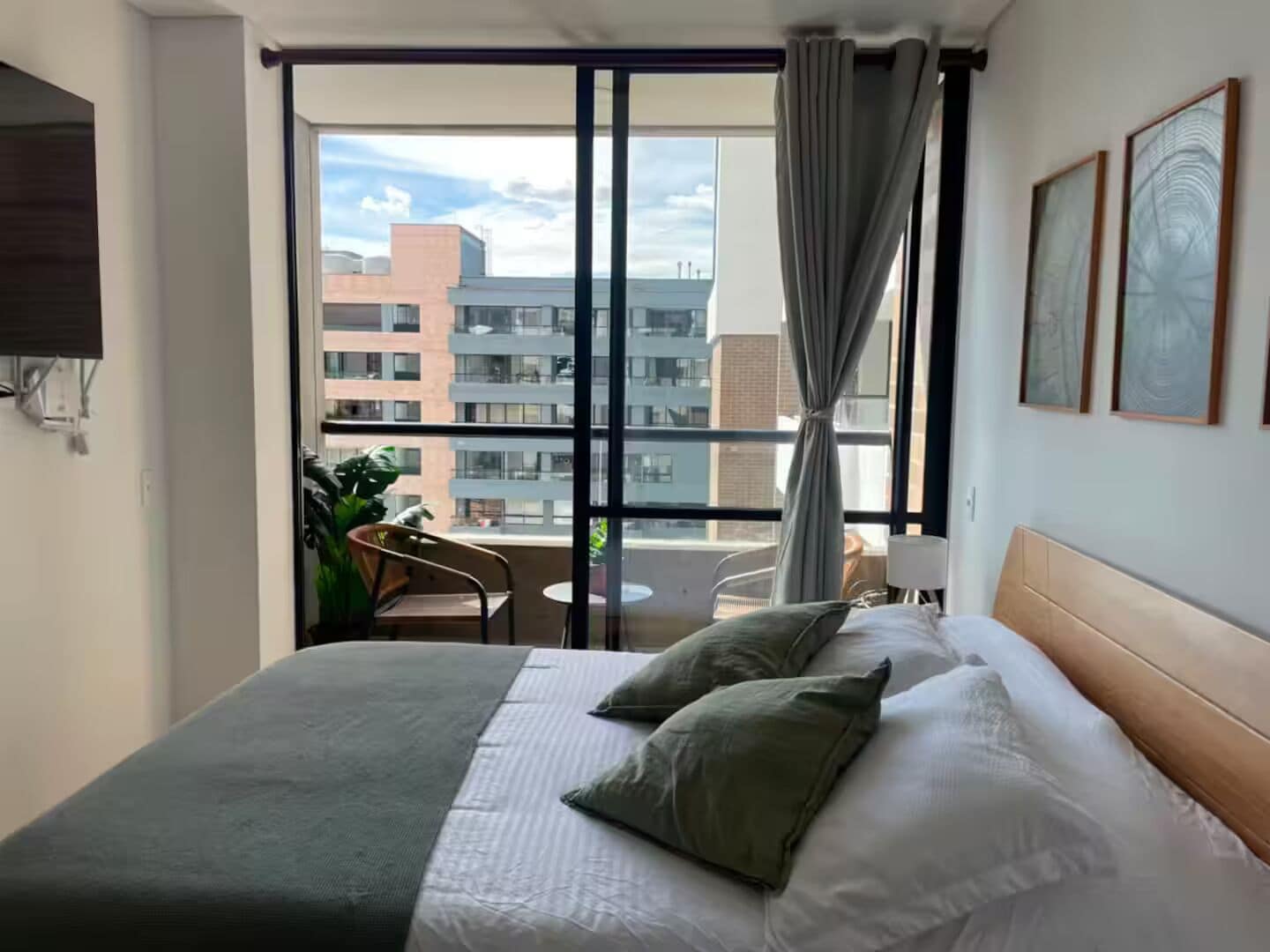 Habitación de hotel con cama, una silla, una mesa y un balcón con vistas a edificios.