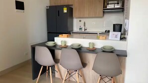 Una cocina moderna con un refrigerador negro, gabinetes de madera, un lavamanos de acero inoxidable y taburetes de bar.