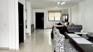 A modern living room with a sofa, a dining table, and a large window with blinds. - House with Private Pool, BBQ, and Jacuzzi in Guayaquil's Social District (Milann Turin)