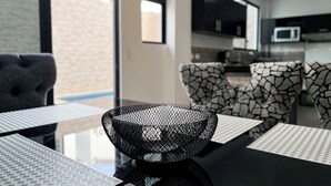 A modern living area with a dining table, patterned chairs, a black woven bowl, and a kitchen in the background. - House with Private Pool, BBQ, and Jacuzzi in Guayaquil's Social District (Milann Turin)
