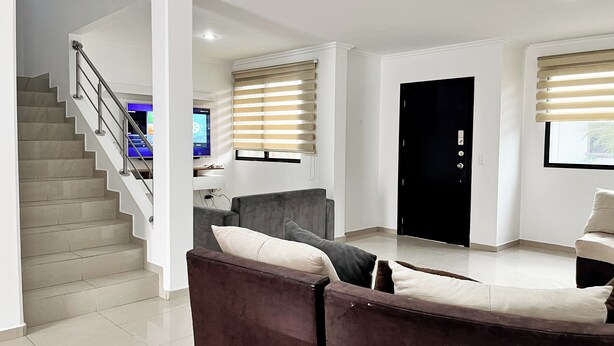 A modern living room with a staircase, a grey sofa, a black door, and a window with blinds. - House with Private Pool, BBQ, and Jacuzzi in Guayaquil's Social District (Milann Turin)