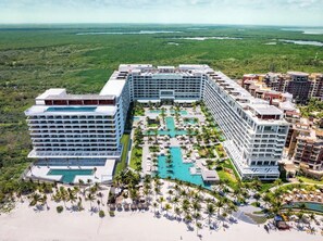 A large hotel with multiple buildings, a central swimming pool, and surrounding palm trees. - Luxury Oceanfront Studio King Bed / Garza Blanca Cancun / Optional All-Inclusive (Cancun)