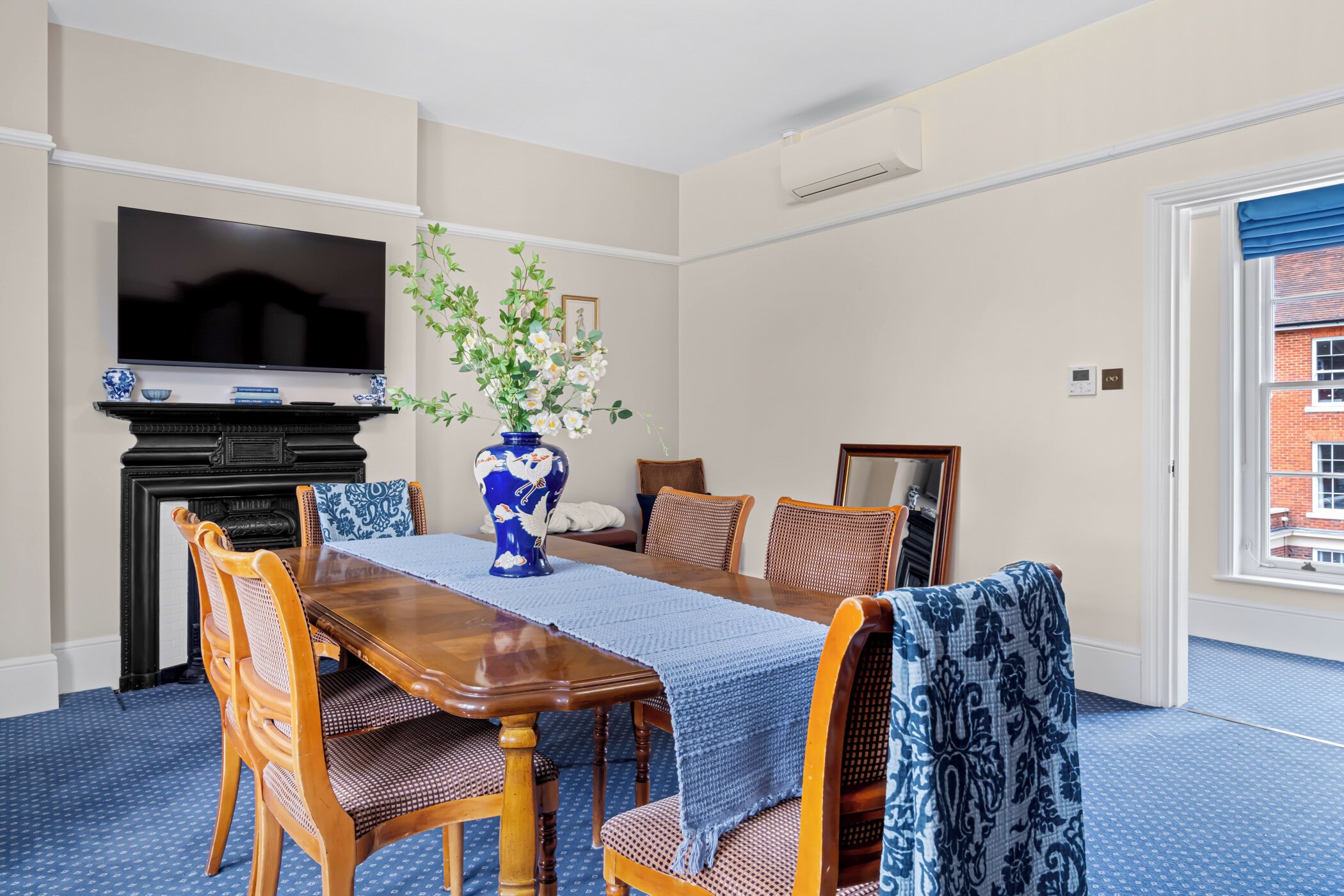 Une salle à manger avec une table en bois, des chaises, un vase de fleurs, un téléviseur à écran plat et une cheminée.