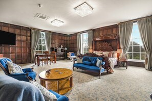 A room with a large bed, a blue sofa, a wooden coffee table, a TV mounted on the wall, and a window with curtains. - West Court Retreat (Wokingham)
