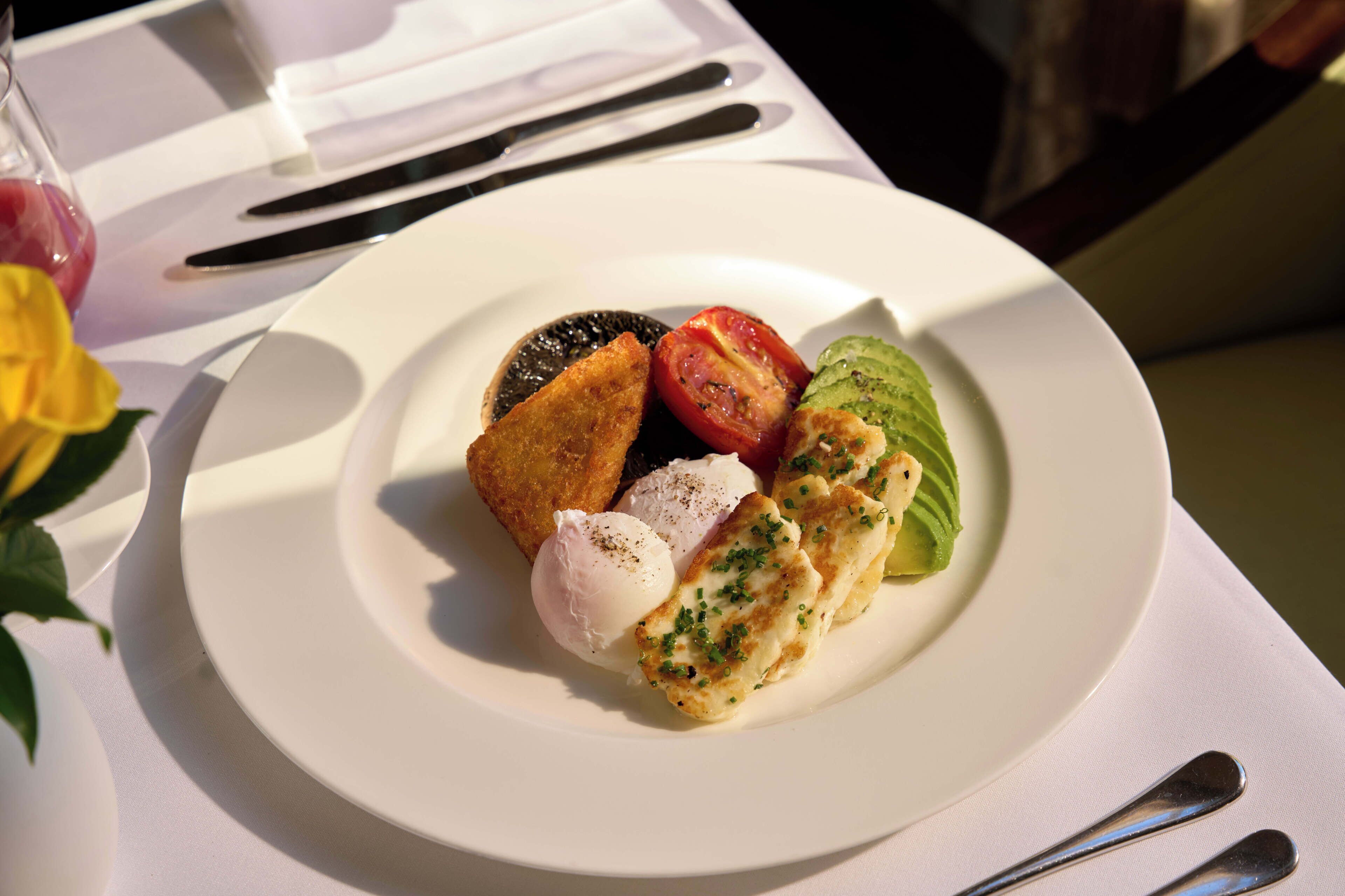 Un plato con un huevo escalfado, una rodaja de tomate, una rebanada de pan y una loncha de aguacate sobre un plato blanco.