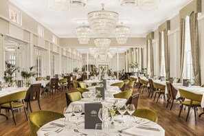 A spacious dining hall with multiple tables, chandeliers, and a long view corridor. - West Court Retreat (Wokingham)
