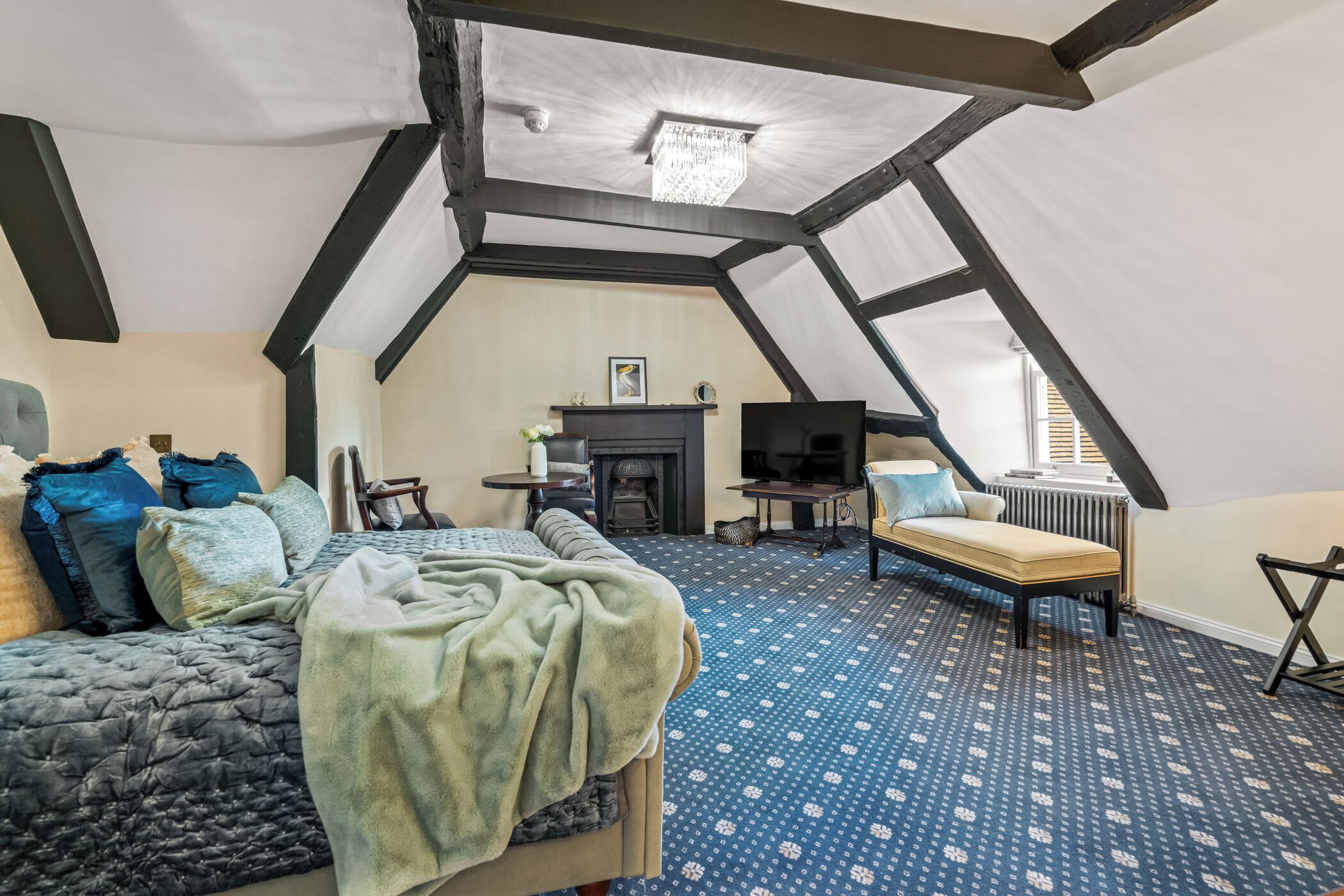 A bedroom with a sloped ceiling, a bed, a chair, a television, and a fireplace.