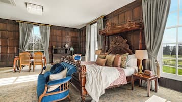 Une chambre avec un grand lit, un canapé bleu, une tête de lit en bois, une table de chevet avec une lampe et une vue sur l’extérieur.