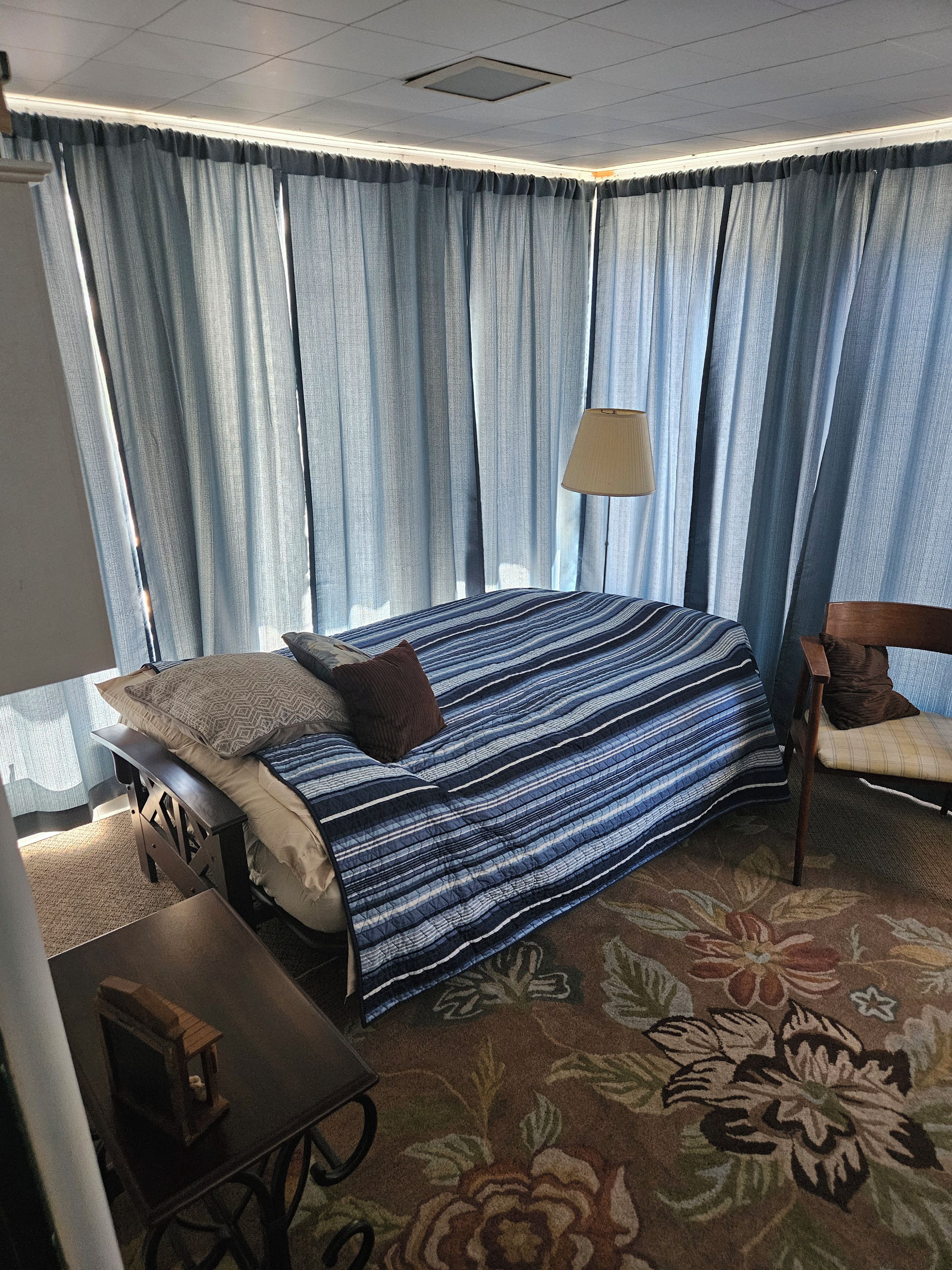 A hotel room with a bed, a chair, a table, and curtains.