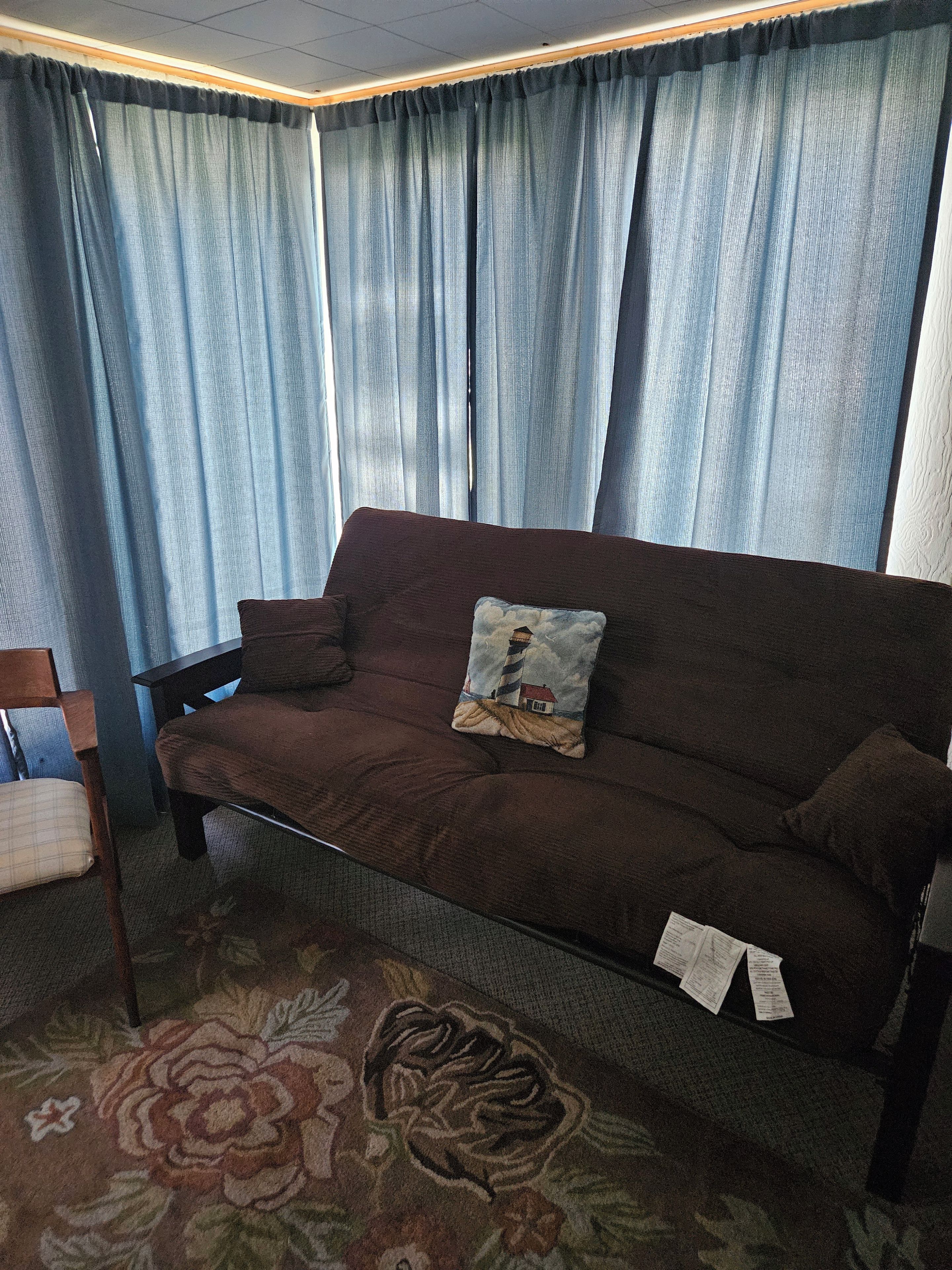 A brown sofa with a cushion, a floral carpet, and a window with blue curtains.