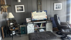 Olohuone, jossa on televisio, työpöytä, tuoli, matto ja seinäkoristeita.