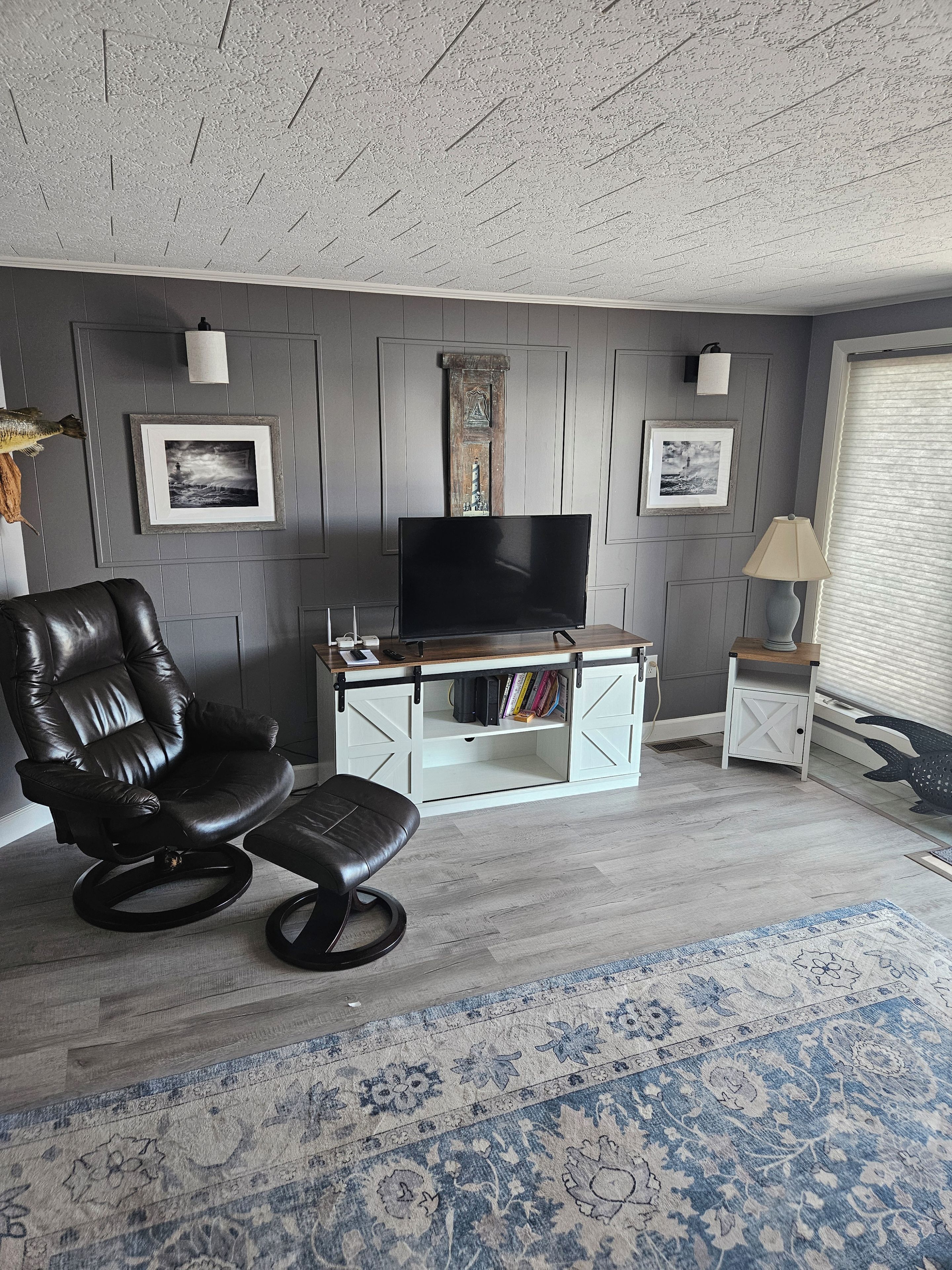 Ein Wohnzimmer mit Ledersessel, Flachbildfernseher, weißem Schrank und einem Teppich mit Muster.