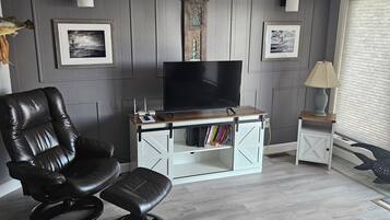 Ein Wohnzimmer mit Ledersessel, Flachbildfernseher, weißem Schrank und einem Teppich mit Muster.
