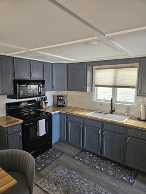A modern kitchen with grey cabinets, a black stove, and a window with blinds.
