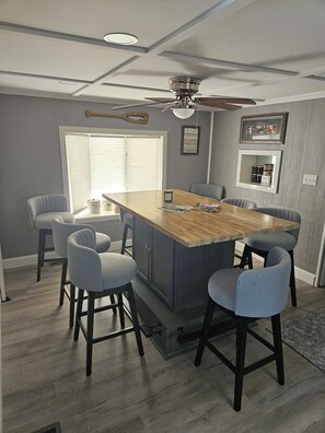 A modern kitchen with a central island, grey upholstered chairs, a ceiling fan, and a window with blinds. - Peaceful 3-bedroom waterfront house with AC on charming Sodus Bay (Sodus Point)