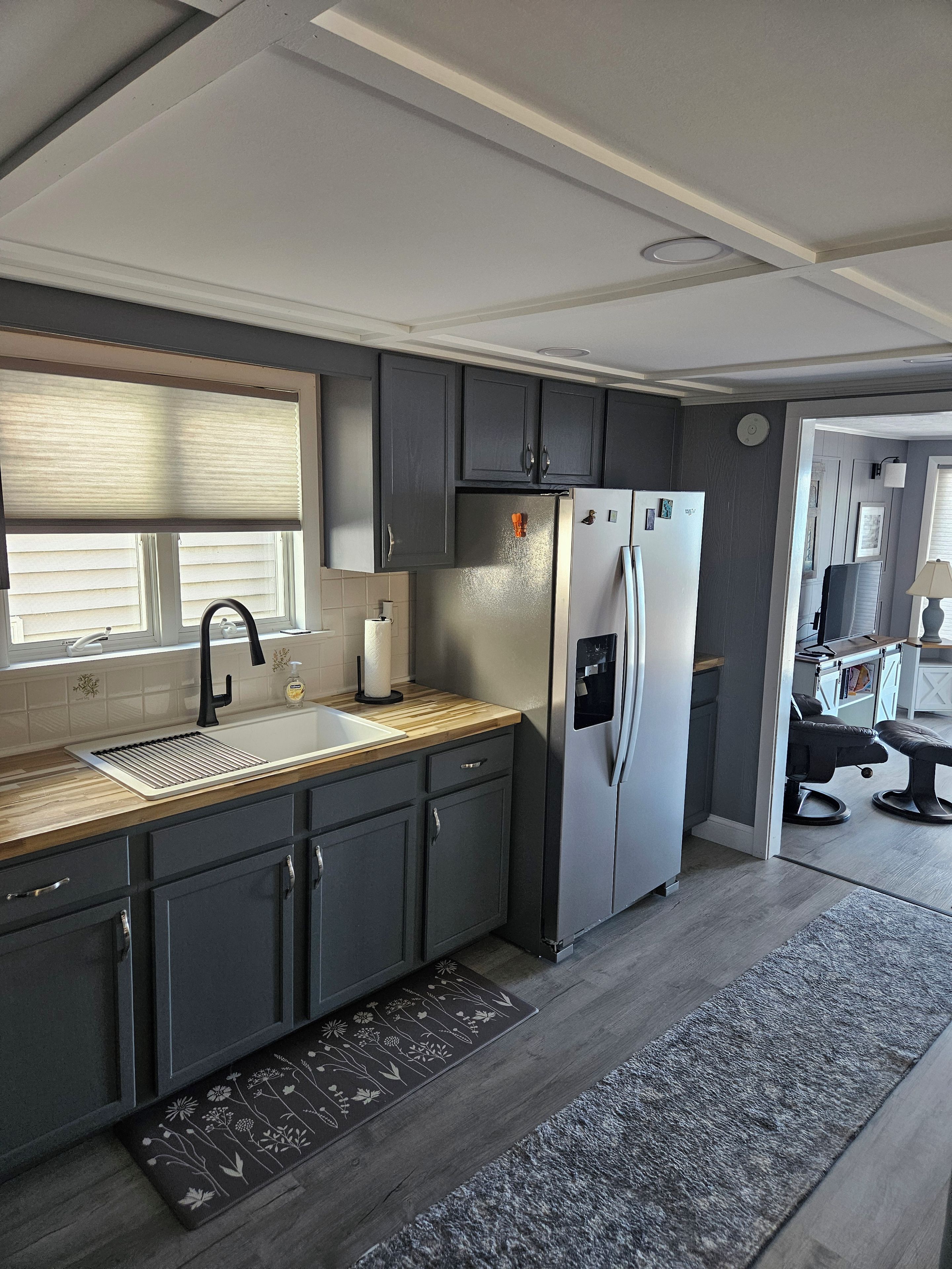 Une cuisine moderne avec des meubles de couleur sombre, un réfrigérateur en acier inoxydable et un plan de travail en bois.