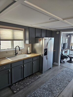 A modern kitchen with dark cabinets, a stainless steel refrigerator, and a wooden countertop. - Peaceful 3-bedroom waterfront house with AC on charming Sodus Bay (Sodus Point)