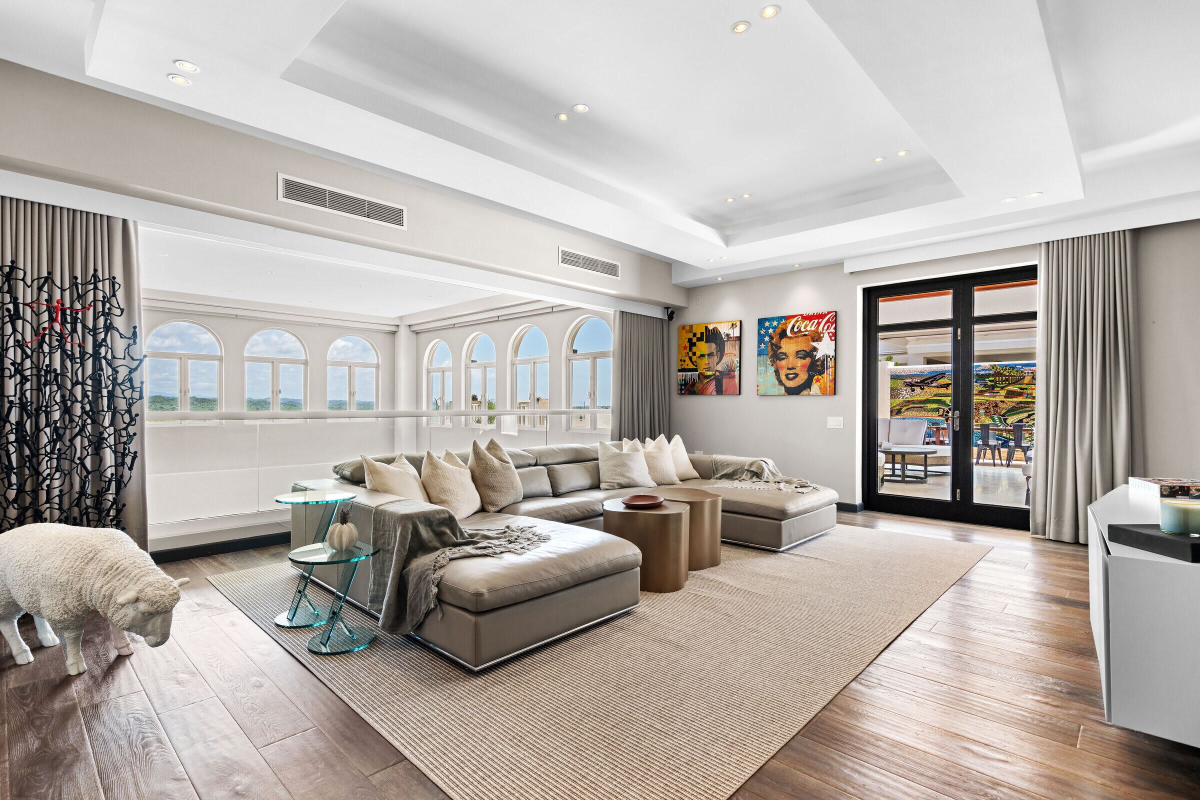A spacious living room with a sectional sofa, a glass coffee table, and a large window with arched tops.