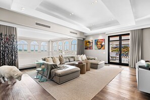 Ein geräumiges Wohnzimmer mit einer Eckcouch, einem Glastisch und einem großen Fenster mit Rundbögen.