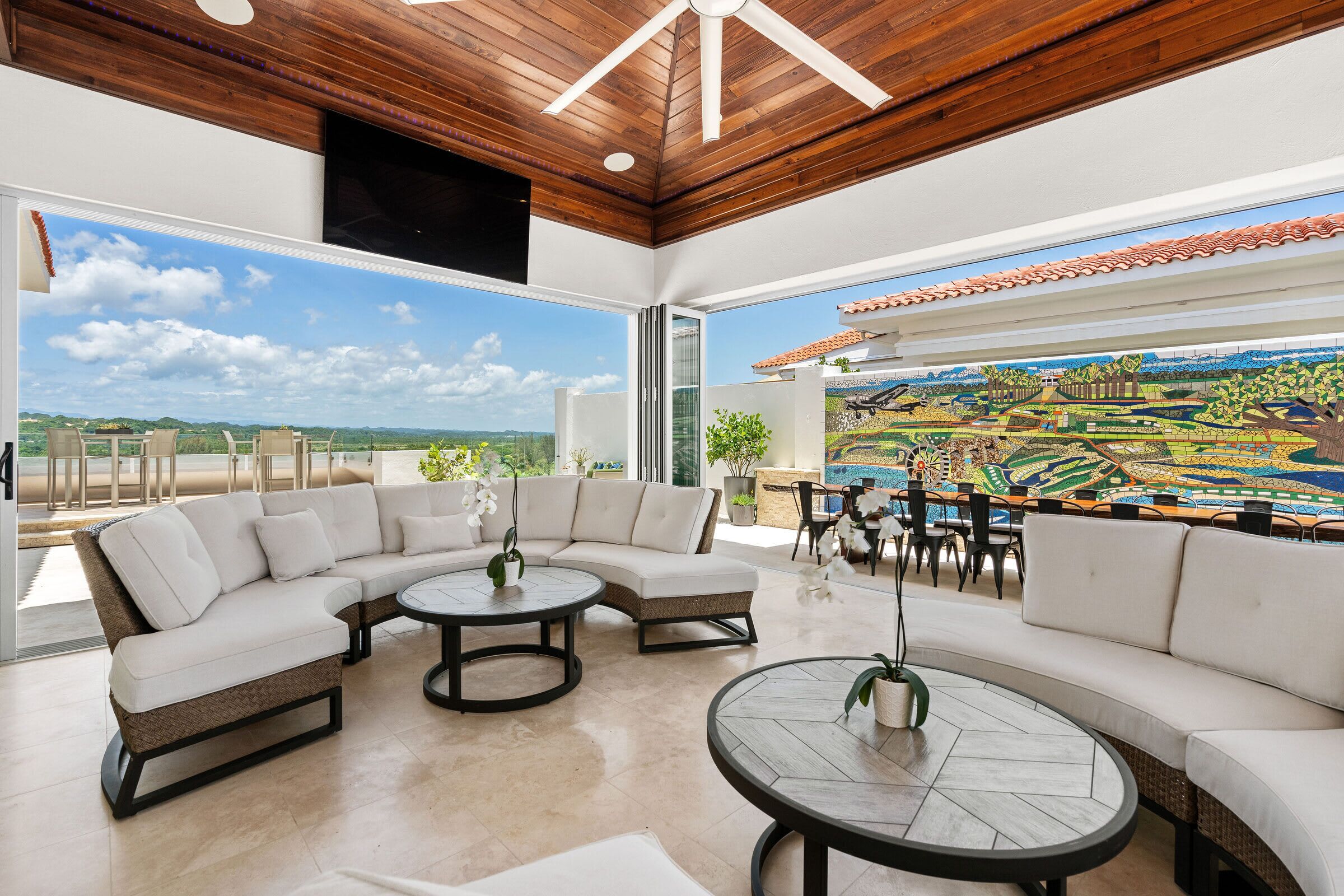 A modern living room with a sectional sofa, round coffee tables, and a large window with a view of a landscape.