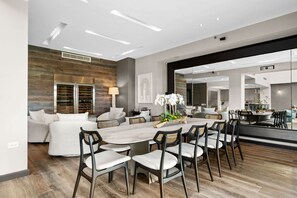 Ein modernes Wohnzimmer mit einem großen Esstisch, weißen Sofas und einer durch einen offenen Durchgang sichtbaren Küche.