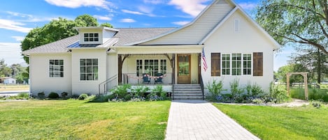 A two-story house with a front porch, a flag, and a brick pathway leading to the entrance.