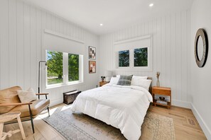 Ein Schlafzimmer mit einem großen Bett, einem Holfnachtkästchen, einem Beistelltisch, einem Fenster und einem wandmontierten Spiegel.