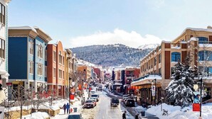 A snow-covered street with buildings, a mountain in the background, and a sign for 'Park City.' - Spring break Ski trip at Park City!! (Park City)