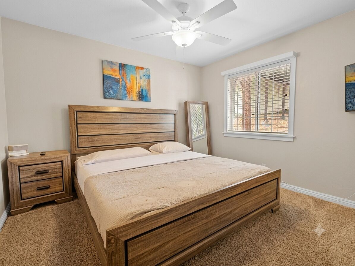 A bedroom with a wooden bed, a nightstand, a ceiling fan, and a window with blinds.