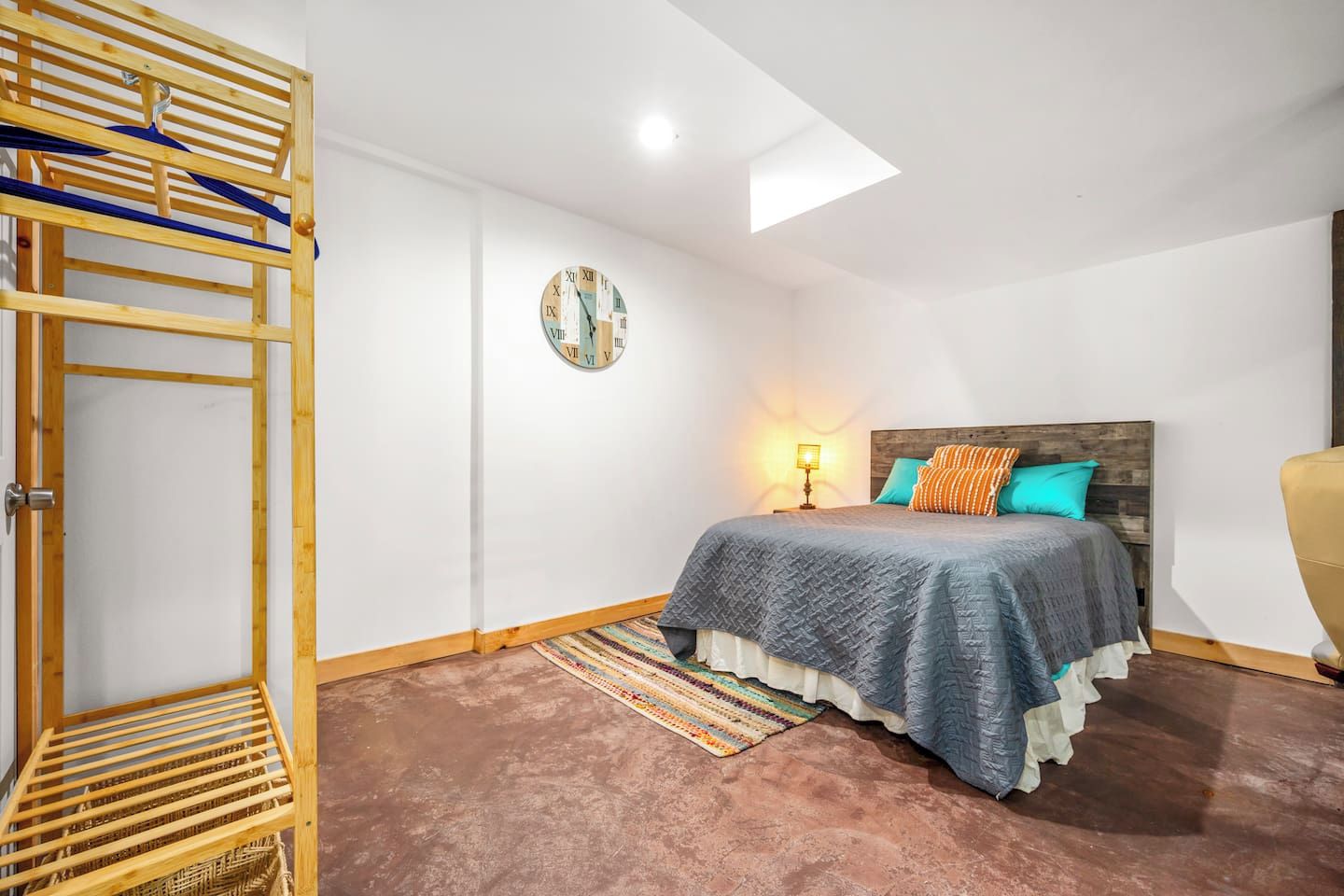 A bedroom with a bed, a wooden headboard, a wall clock, a hanging rack, and a skylight.