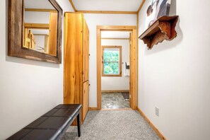 A hallway with a bench, wooden door, and a small window with a view of greenery.