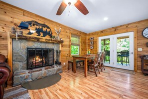 L’intérieur chaleureux d’un chalet avec une cheminée en pierre, des murs en bois, un coin repas et un ventilateur de plafond.