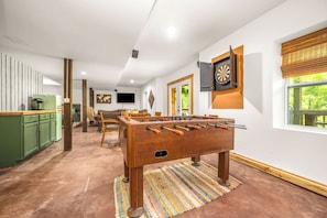 A room with a foosball table, a dartboard, and a television.