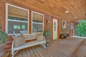 A wooden cabin with a covered porch, a bench with cushions, and a door with a sign.