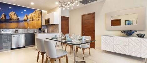 Una cocina moderna con una mesa de comedor de vidrio, armarios blancos y un salpicadero decorativo.