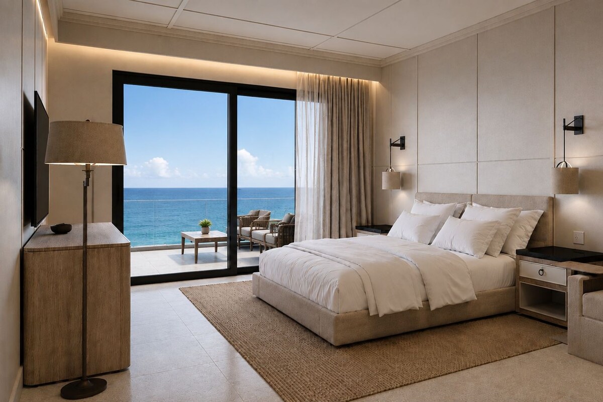 A modern hotel room with a large bed, a desk, a sofa, and a view of the sea.