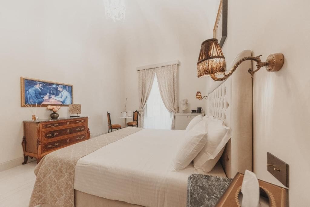 A bedroom with a bed, dresser, lamp, and artwork on the wall.