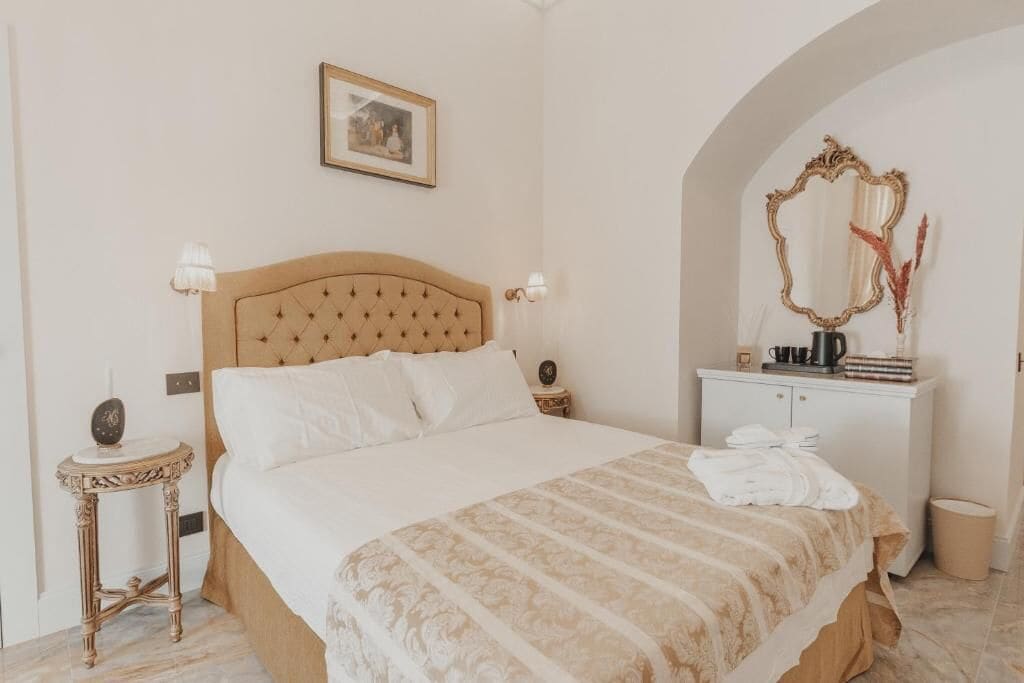 Een slaapkamer met een groot bed, een nachtkastje met een lamp, een kaptafel met spiegel en een lijst met een foto aan de muur.