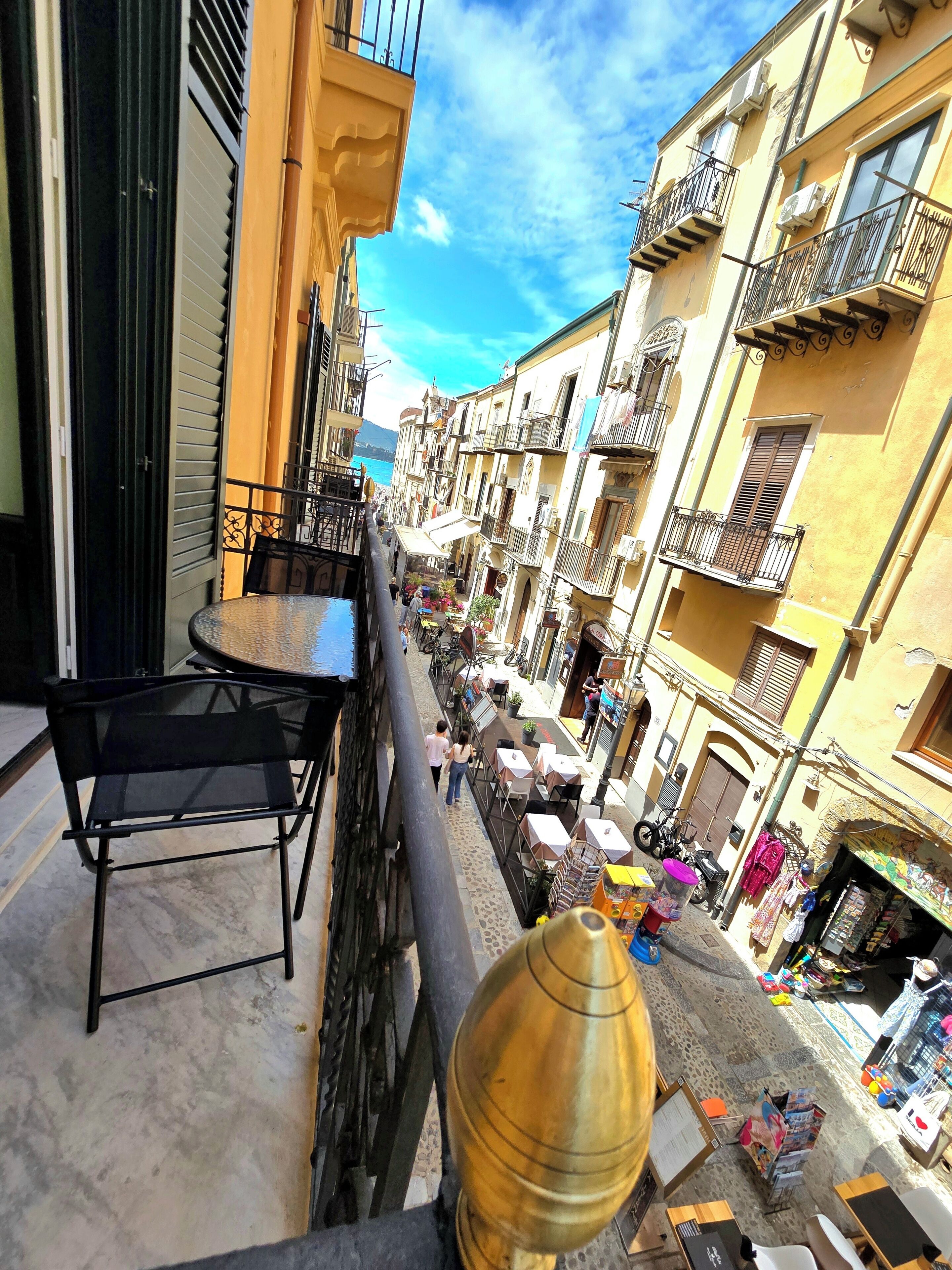 Una calle estrecha con balcones, mesas al aire libre y tiendas.