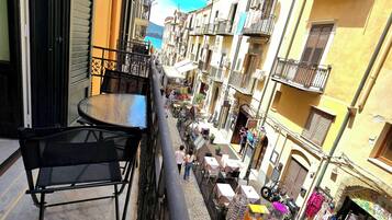 Una calle estrecha con balcones, mesas al aire libre y tiendas.