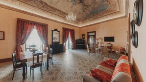 Une pièce comprenant une table à manger, des chaises, un canapé, un piano et un lustre.