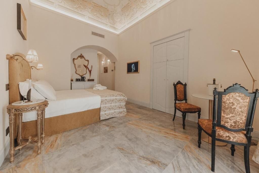 A bedroom with a bed, a vanity with a mirror, a chair, a table, and a wardrobe.