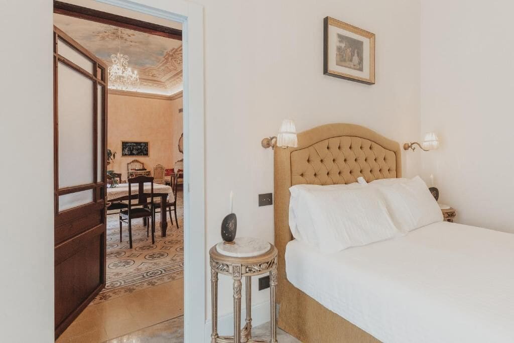 A hotel room with a bed, bedside table, and a chandelier.