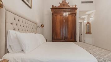 Un dormitorio con cabecera capitonada, un amplio armario de madera, cama con ropa blanca y alfombra estampada.