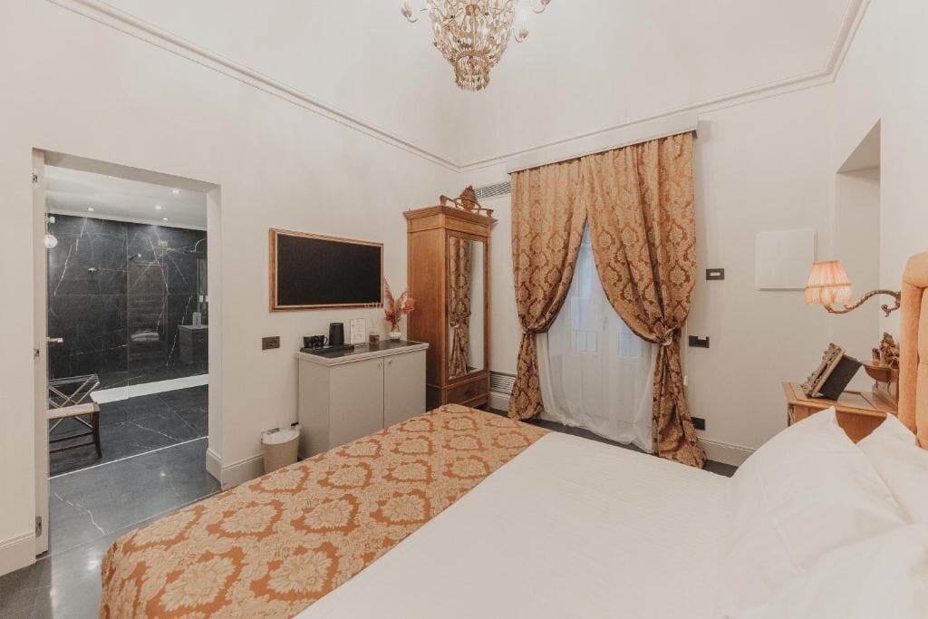 Habitación de hotel con cama, escritorio, tocador, espejo, candelabro y baño con ducha.