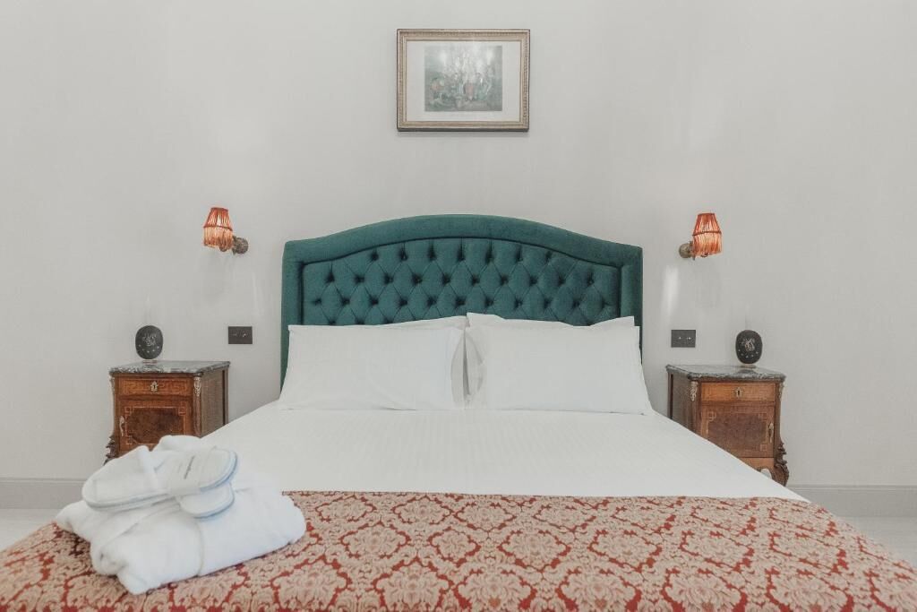 A neatly made bed with a green headboard, white pillows, and a red patterned bedspread. There are two wooden nightstands with lamps on either side of the bed.