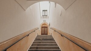 Una escalera con barandilla de madera, una puerta de madera al final e una pared blanca.